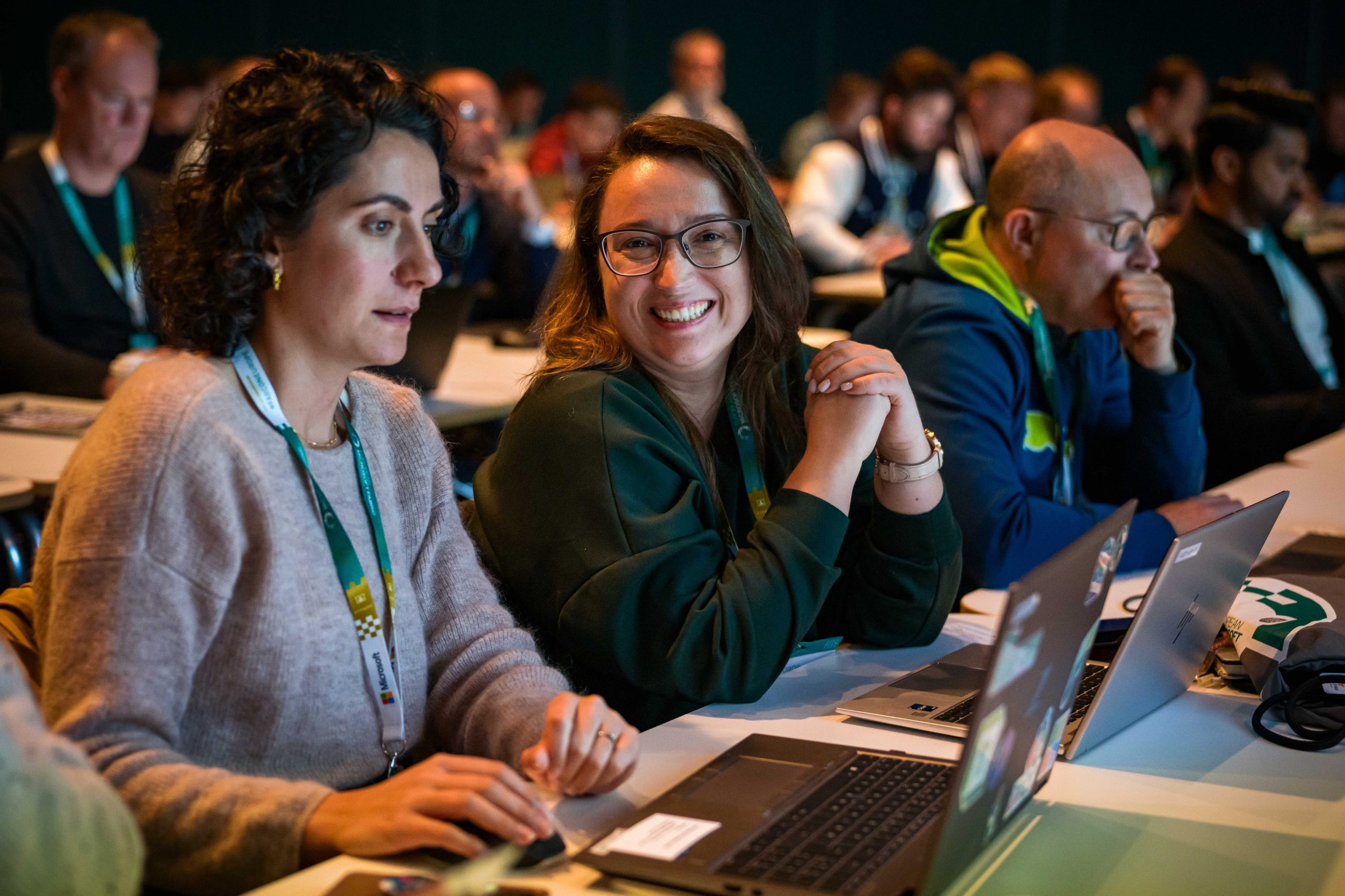woman smiles for the camera while working at a laptop in a conference session room