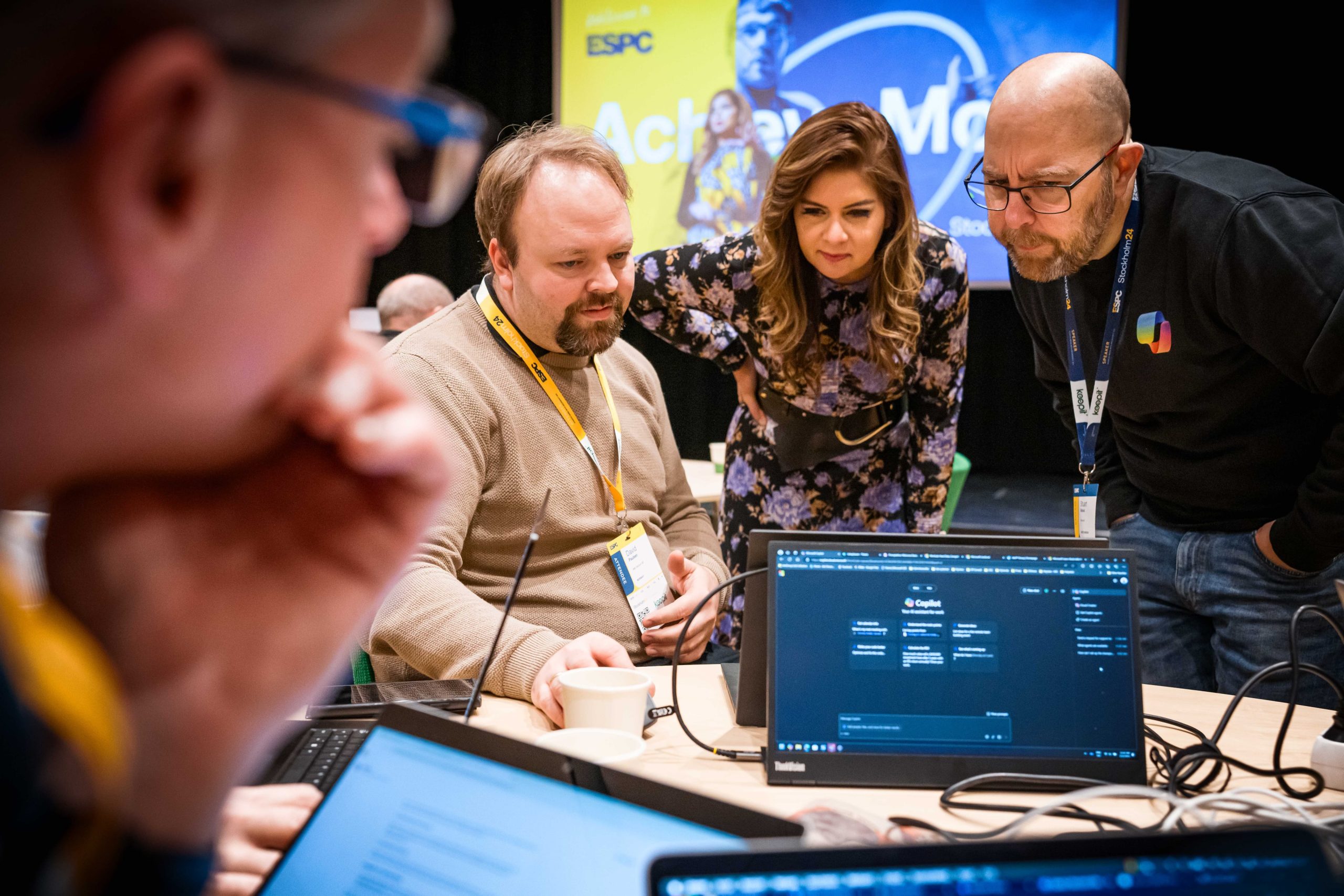 a group of people huddle together while looking at a laptop screen during a conference workshop session
