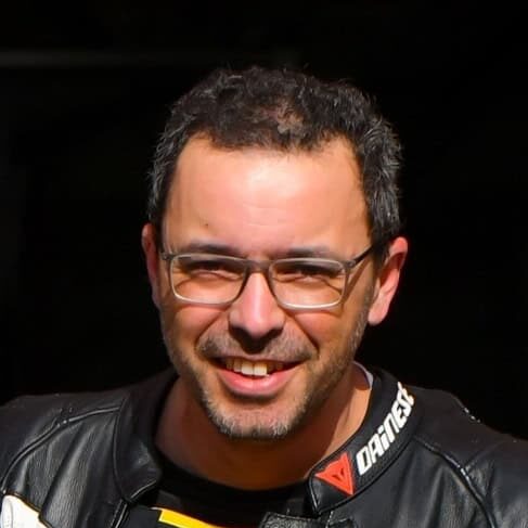 A person in a dark setting is wearing a motorcycle jacket with visible branding on the collar and shoulders. The background is black, and the scene is dimly lit.