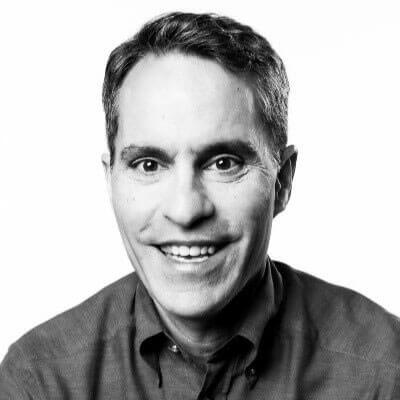 A person shown from the shoulders up in a black‑and‑white portrait, wearing a collared shirt, with a plain background