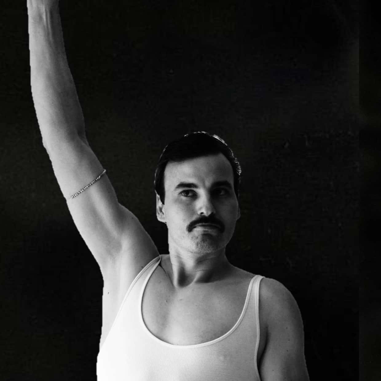 A person photographed in black and white, raising one arm while wearing a sleeveless top against a dark background.