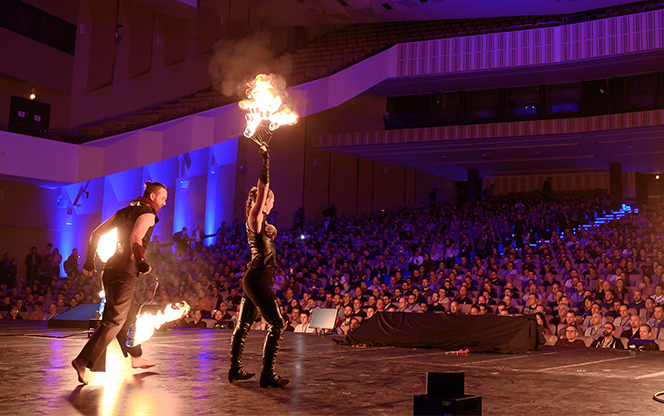 fire dancers perform on the main stage to a full auditorium before a conference keynote