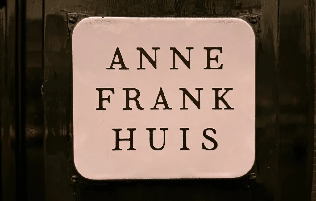 White rectangular sign with black text reading ‘Anne Frank Huis’ mounted on a dark door.