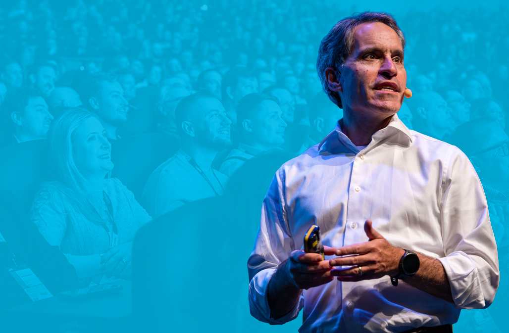 Jeff Teper speaking during a keynote - in the background is a faded image of the audience smiling