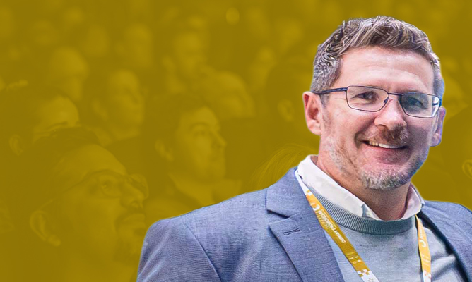 FabCon sponsor Alan Haefele smiles for the camera over a background of a sitting audience